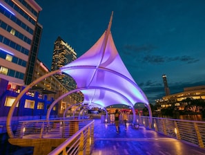 A waterfront promenade with a modern canopy structure, a bridge, and a city skyline in the background. - Cozy Retreat Mins To Riverwalk, TGH, RJS, UTampa, TPA, Beach (Tampa)