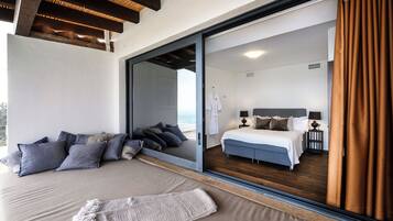 Un dormitorio con un amplio ventanal corredera que da a un balcón, una cama con cabecera gris y una mesita de noche con lámparas.