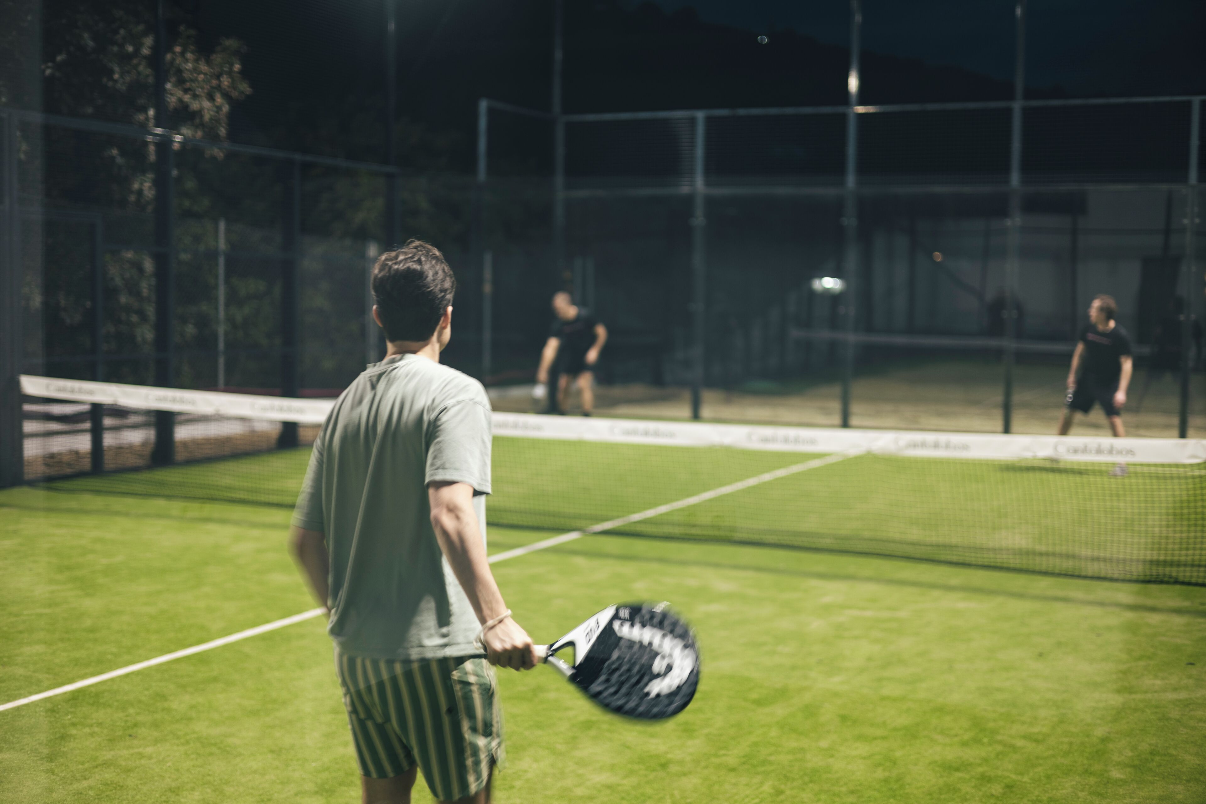 Una cancha de tenis con una red, un jugador en primer plano y otro al fondo.