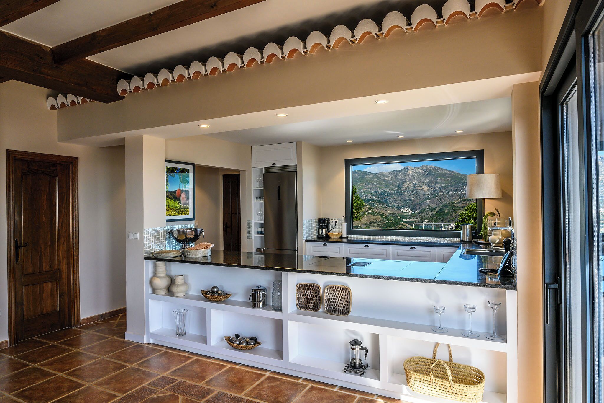 A modern kitchen with a large island, a view of a mountain, and a wooden door.