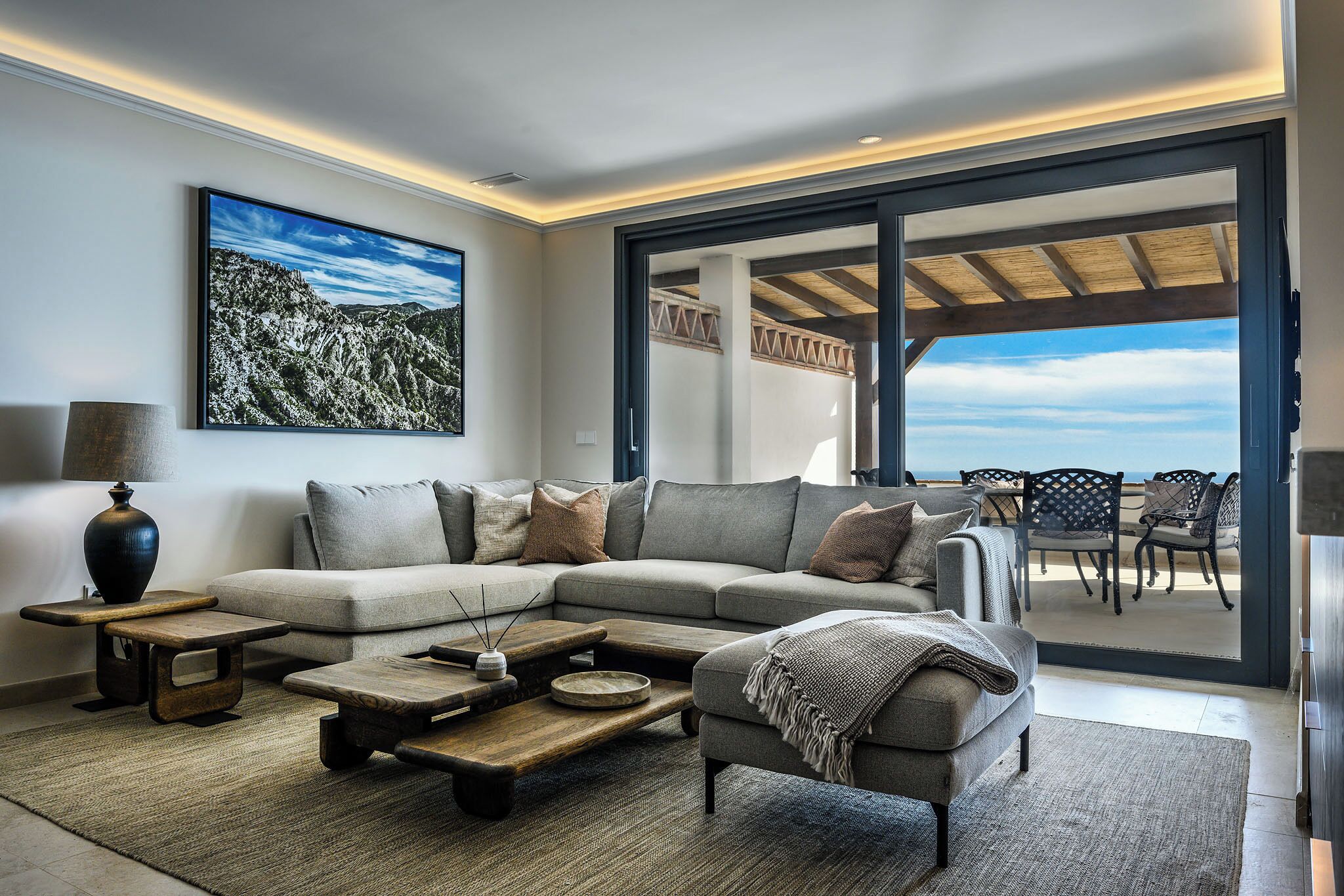 Ein modernes Wohnzimmer mit einem Ecksofa, Couchtisch und großem Fenster mit Blick auf eine Terrasse.
