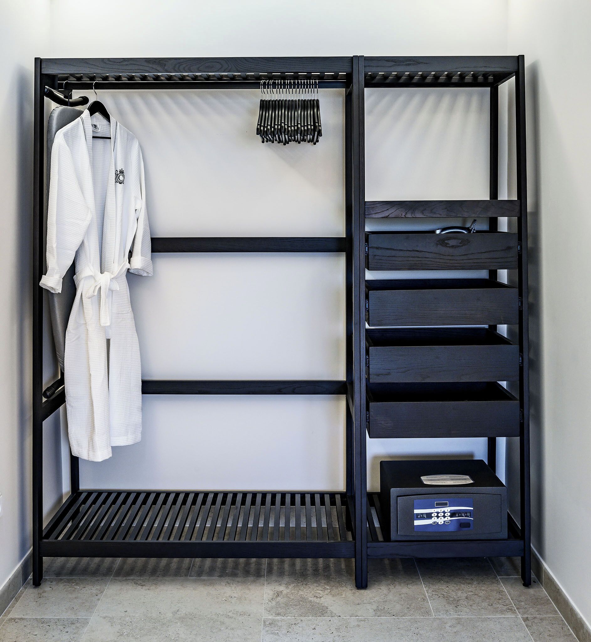 A black metal wardrobe with multiple shelves and a hanging rod, containing a white robe and a small electronic device.