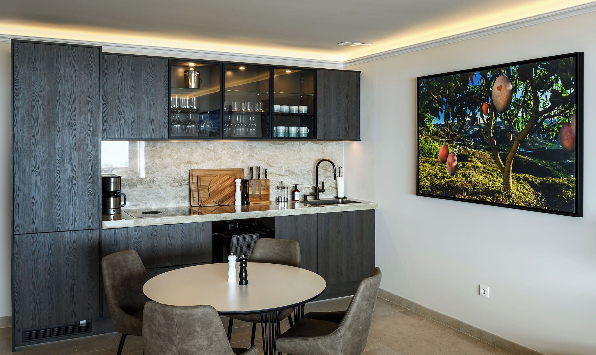Una cocina moderna con armarios de madera oscura, encimera de mármol y una zona de comedor con una mesa redonda y sillas.