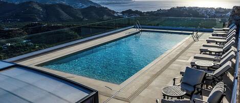 A rooftop pool with clear blue water, surrounded by lounge chairs and a glass balustrade.