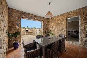 A stone-walled dining area with a table and chairs, a hanging light fixture, and a view of the outdoors. - Holiday Home 'La Chumbera' with Shared Pool and Private Terrace (Vejer de la Frontera)