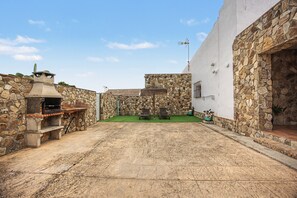 Un patio con muro de piedra, una parrilla y un pequeño espacio con asientos.