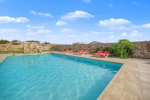 A swimming pool with clear blue water, surrounded by stone walls and red lounge chairs. - Holiday Home 'La Chumbera' with Shared Pool and Private Terrace (Vejer de la Frontera)