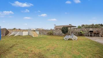 Un patio trasero con un muro de piedra, una parrilla y un conjunto de sillones de descanso.