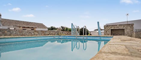 Une piscine avec un mur en pierre et, au fond, un bâtiment dont le toit est recouvert de tuiles.