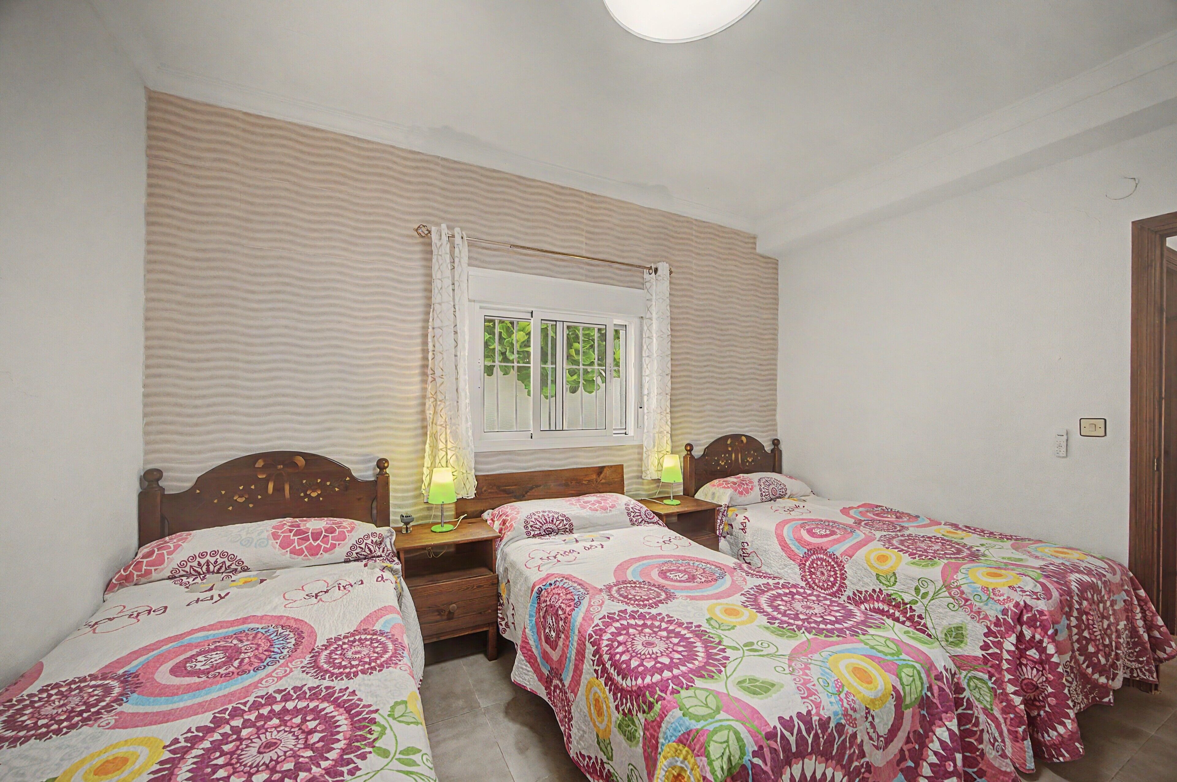 Una habitación con dos camas individuales, una ventana con cortinas, una mesita de noche con lámpara y un espejo instalado en la pared.