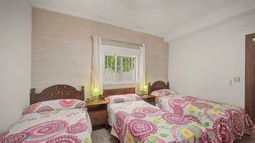 Una habitación con dos camas individuales, una ventana con cortinas, una mesita de noche con lámpara y un espejo instalado en la pared.