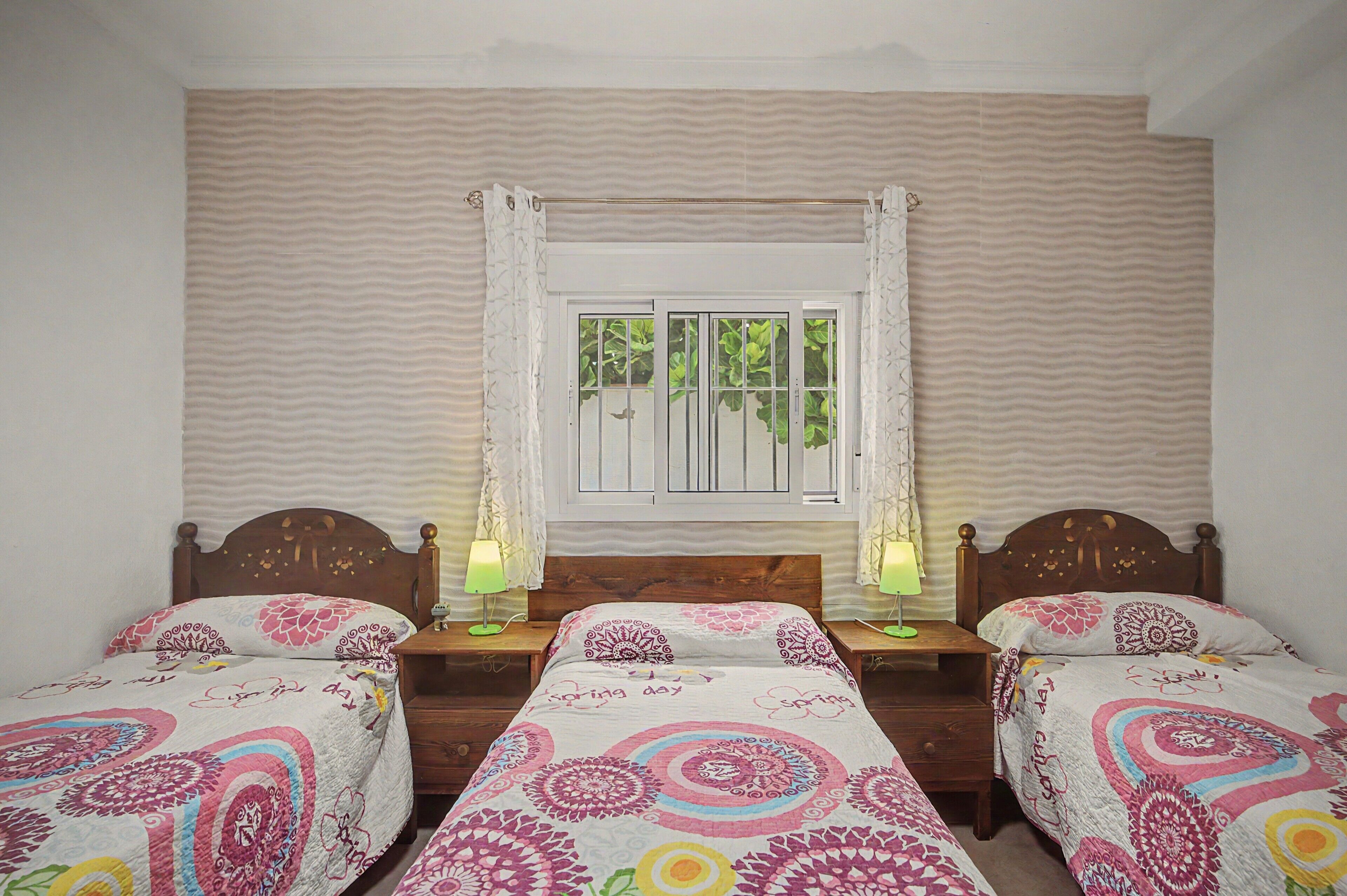 Ein Zimmer mit zwei Einzelbetten, einem fensterbelaubten Fenster und einer Wand mit einem Wellenmuster.