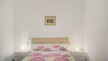 Un dormitorio con cama, dos mesitas de noche, lámpara de noche y un cuadro en la pared.