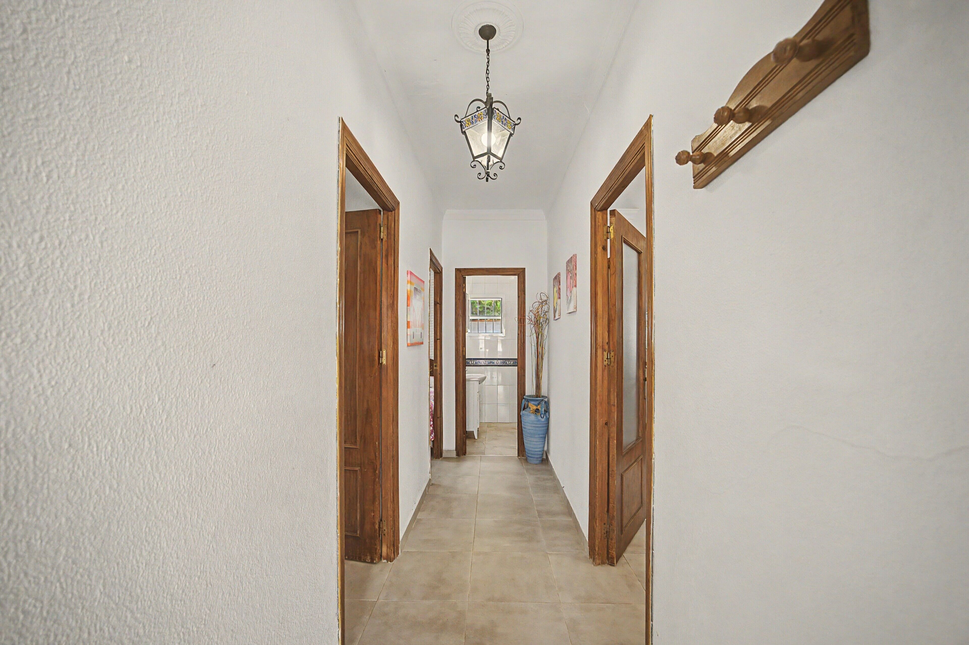 Un pasillo con puertas de madera, piso de baldosas y una lámpara colgante.