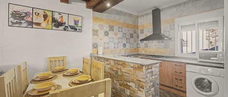 Eine Küche mit einer Steinservierinsel, Holzstühlen, einer integrierten Waschmaschine und einer Fliesenküchenrückwand.