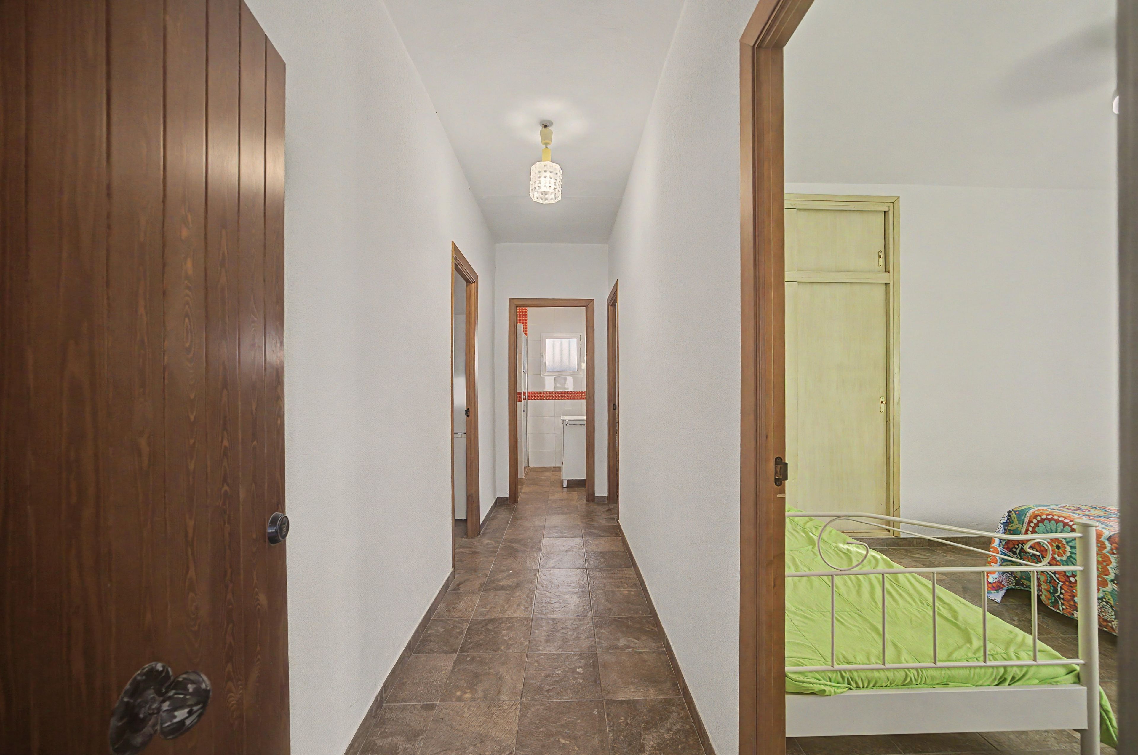 A hallway with wooden doors, a tiled floor, and a bed with a green bedspread.