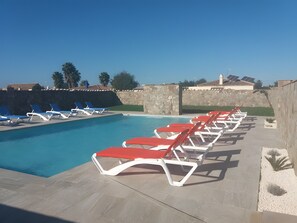 Una piscina con tumbonas, un muro de piedra y cielo despejado.