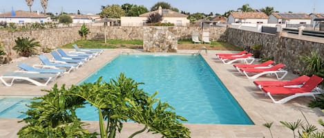 A swimming pool with sun loungers and a stone wall.