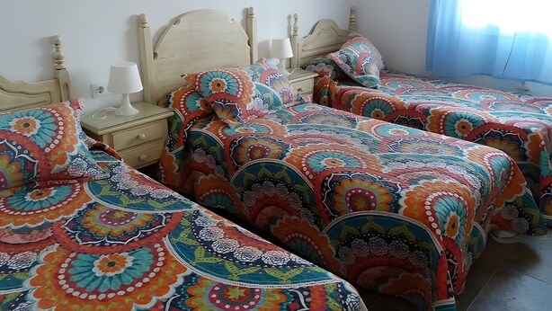 A room with two beds, each with a colorful patterned bedspread, a bedside table with a lamp, and a window with curtains. - Holiday Home 'Casa El Arriate' with Shared Pool and Private Terrace (Vejer de la Frontera)