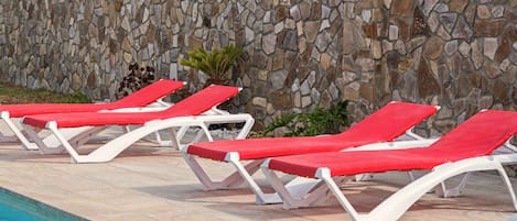 Un espace aménagé au bord de la piscine, avec des chaises longues et un mur en pierre.