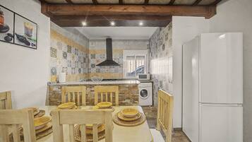 Cocina compacta con comedor, que incluye una isla central, sillas de madera, lavadora integrada y refrigerador blanco.