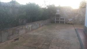 A patio area with a stone wall, a white shelf unit, and a hose on the ground. - Holiday Home 'Casa El Arriate' with Shared Pool and Private Terrace (Vejer de la Frontera)