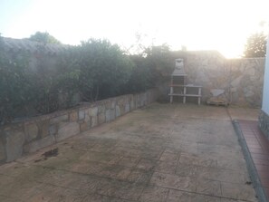 Un patio con un muro de piedra, un estante blanco y una manguera en el suelo.