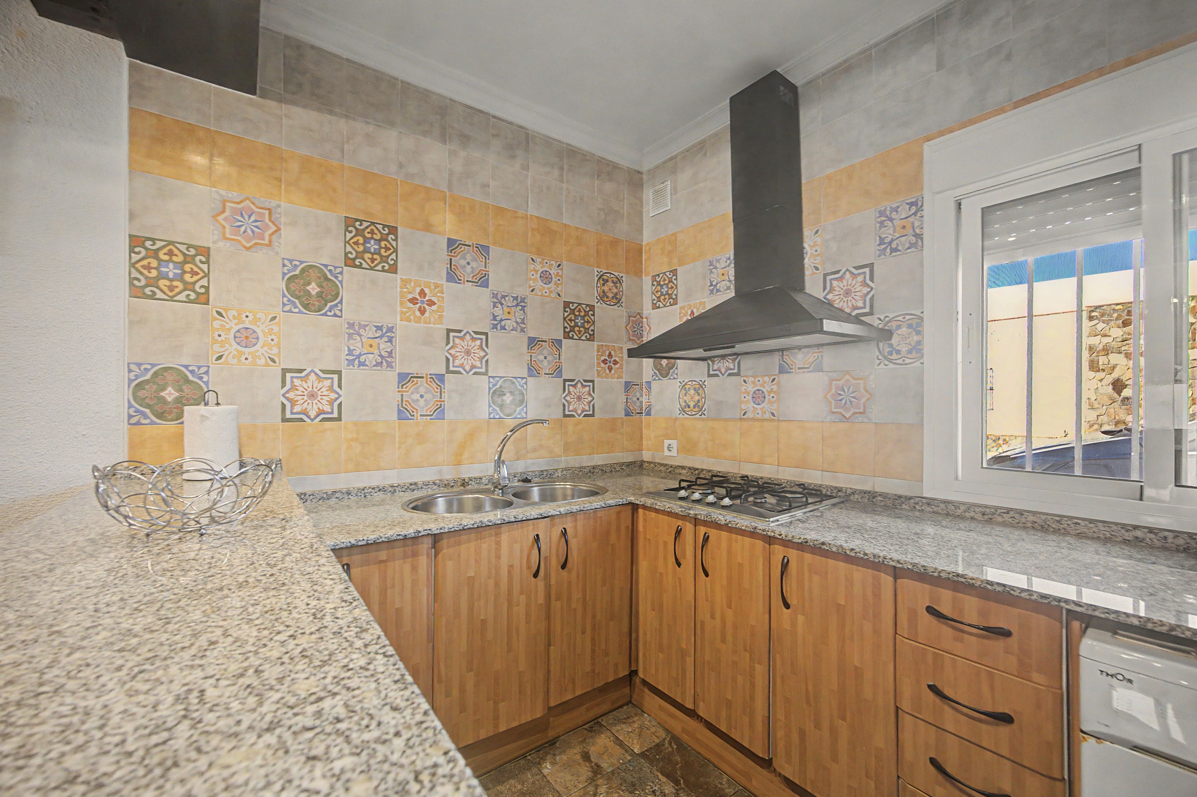 Una cocina con salpicadero de azulejos, armarios de madera, un lavamanos de acero inoxidable y una estufa a gas.