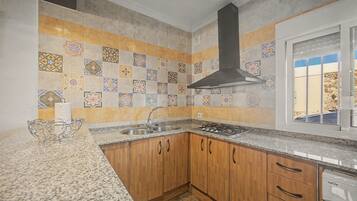 Una cocina con salpicadero de azulejos, armarios de madera, un lavamanos de acero inoxidable y una estufa a gas.