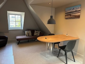 Een modern interieur met een eettafel, stoelen, een bankje, een bank met kussens, een hanglamp en een schilderij aan de muur.