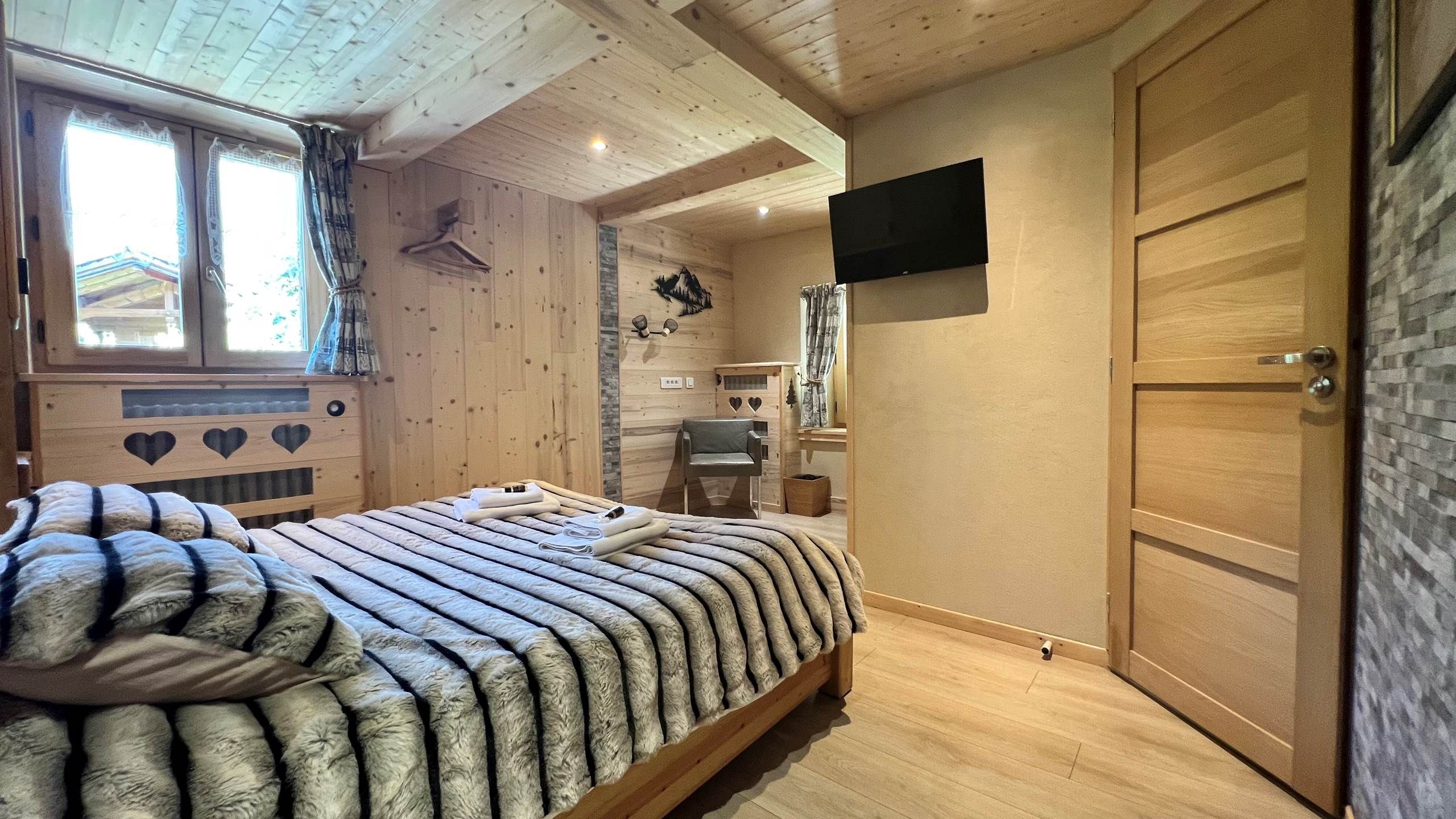 Un intérieur en bois comprenant un lit, un téléviseur fixé au mur et une porte.
