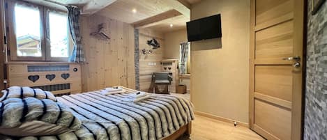 Un intérieur en bois comprenant un lit, un téléviseur fixé au mur et une porte.