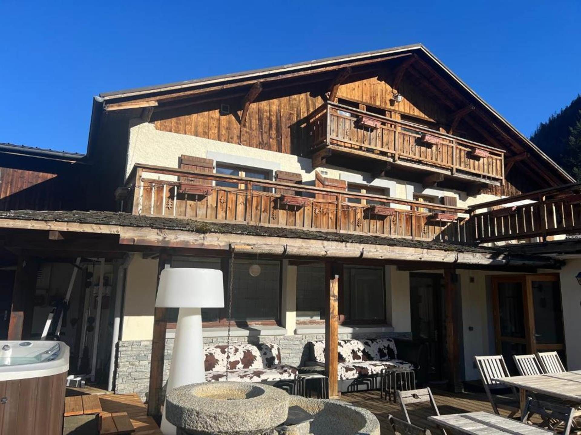 Una cabaña de madera de dos pisos con balcón, mobiliario exterior y un jacuzzi.