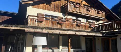 Una cabaña de madera de dos pisos con balcón, mobiliario exterior y un jacuzzi.
