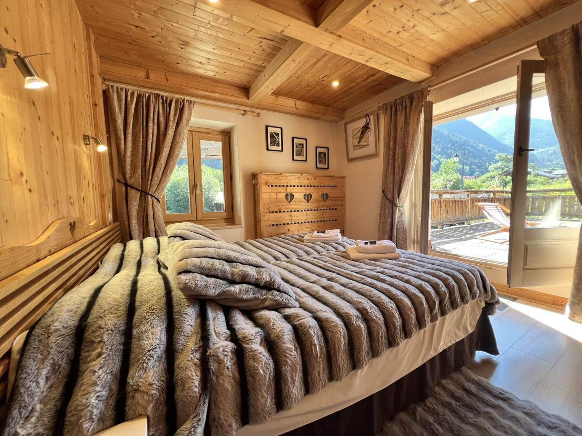 A wooden bedroom with a bed, curtains, a wooden headboard, and a view of the outdoors.