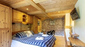 A wooden cabin interior with a bed, a stone wall, and a mounted picture. - Charming chalet (Saint-Gervais-les-Bains)