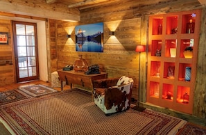 A cozy room with wooden walls, a table with a vase, a cowhide chair, and a red-lit display case. - Charming chalet (Saint-Gervais-les-Bains)