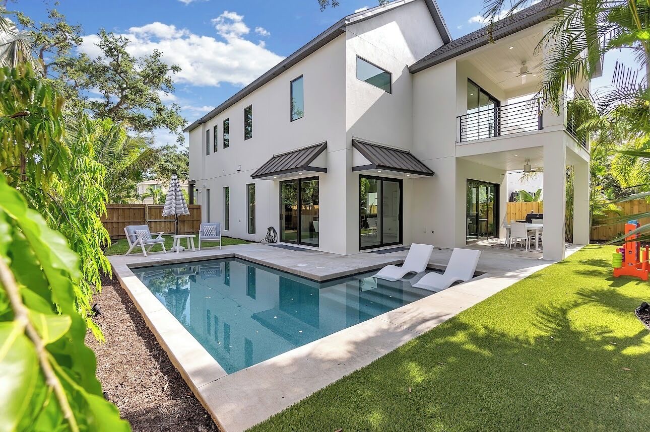 A modern two-story house with a swimming pool, outdoor seating, and a fenced backyard.
