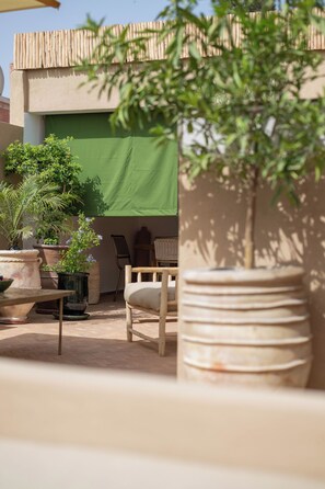 Ein Patio mit Pflanzen in Töpfen, einem Holzstuhl und einem grünen Sonnensegel.