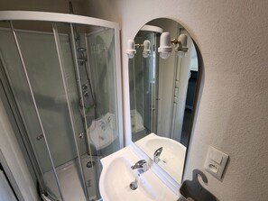 Ein Badezimmer mit einer Duschkabine, einem weißen Waschbecken und einem Spiegel mit gebogenem Oberteil.