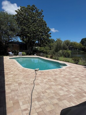 A rectangular swimming pool with a tiled deck, surrounded by lush greenery and a clear blue sky. - 3-bedroom house in beautiful Sarasota with cool AC breeze and heated pool. (Sarasota)