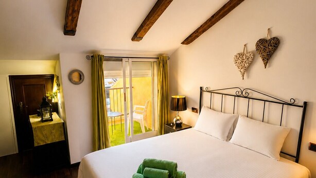 A hotel room with a large bed, wooden beams on the ceiling, a balcony with yellow curtains, and a small table with a lamp. - Villa Jenny – Privates Küstenhaus in Los Alcázares (Los Alcázares)