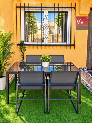 A glass-top table with two chairs, a small potted plant, and a window with a metal grill. - Villa Jenny Private Coastal Retreat Near the Sea (Los Alcázares)