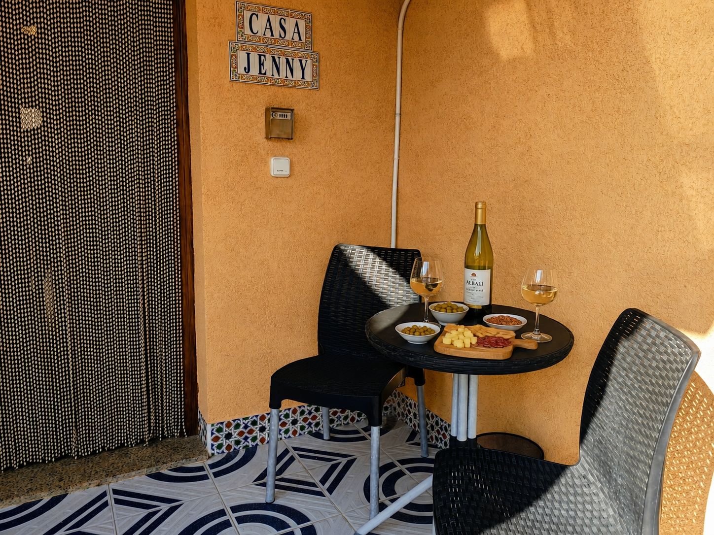 Un petit espace extérieur aménagé avec une table pour deux, une bouteille de vin et un bol d’olives.