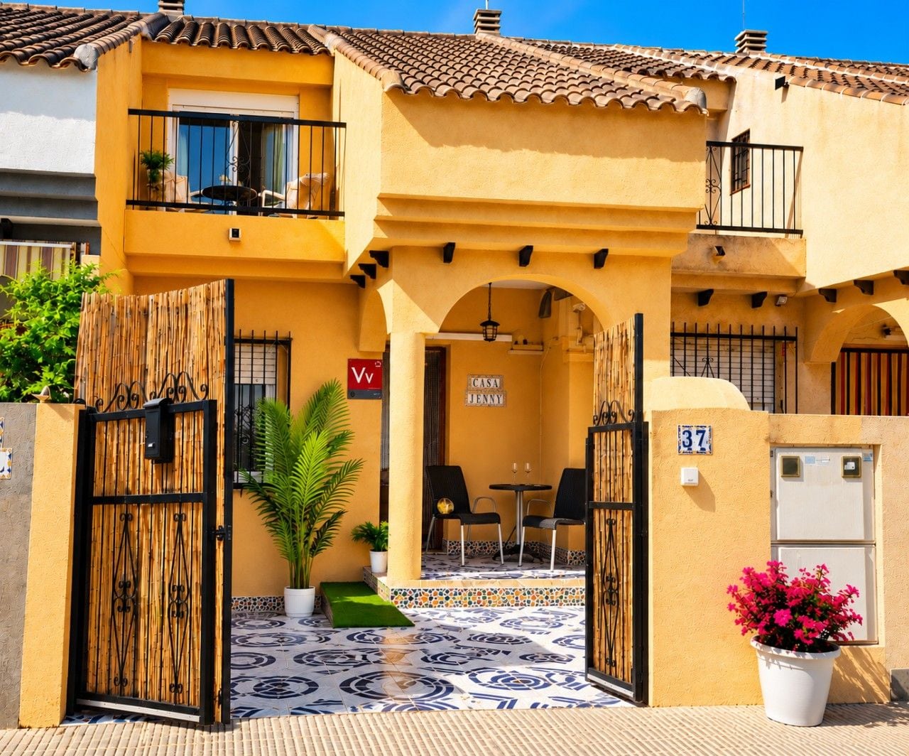 A yellow building with a tiled roof, a gate with a sign, and a potted plant.