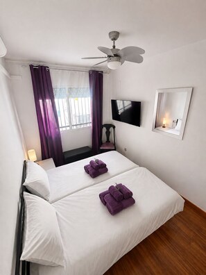 Ein Hotelzimmer mit Bett, Deckenventilator, Fernseher, Spiegel und einem Fenster mit Vorhängen.