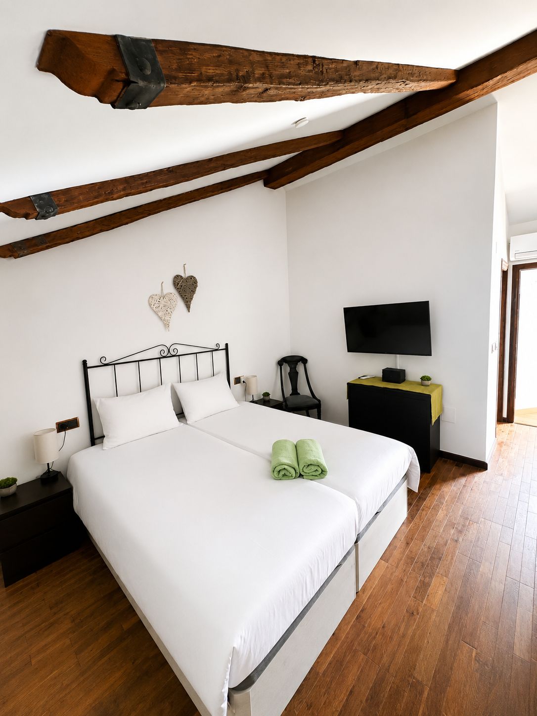 Ein Schlafzimmer mit einem großen Bett, einem Fernseher, einem Schreibtisch und einem Holzbalken an der Decke.