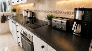 A modern kitchen with white cabinets, a black countertop, a built-in oven, a coffee maker, and a toaster. - Villa Jenny – Privates Küstenhaus in Los Alcázares (Los Alcázares)