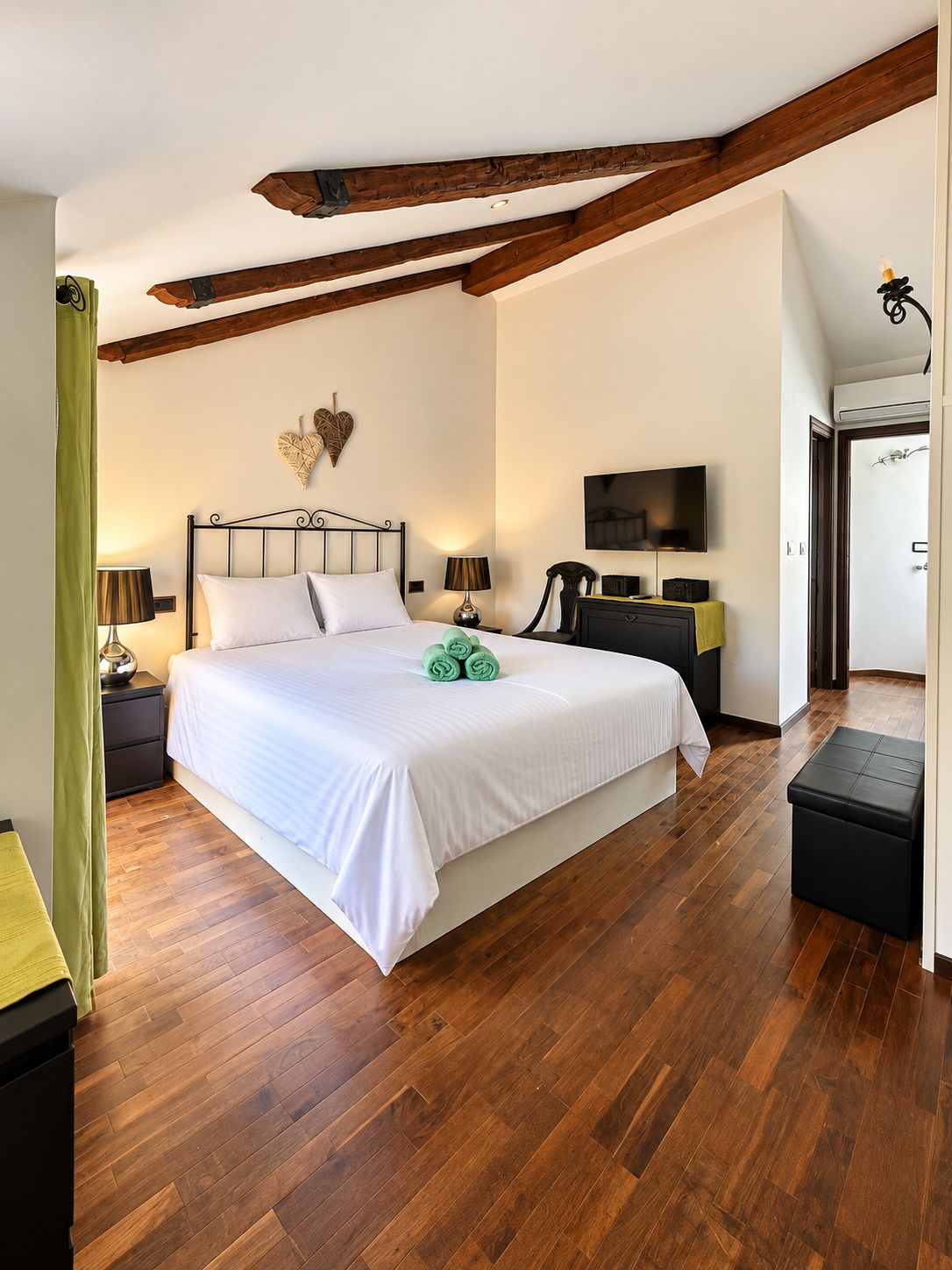 Een slaapkamer met een groot bed, houten balken, een flatscreen televisie en een groene handdoek op het bed.
