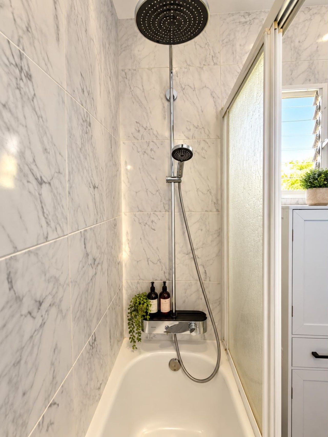 Une salle de bain moderne équipée d’une douche, d’une baignoire et d’une étagère où sont rangés les produits de toilette.